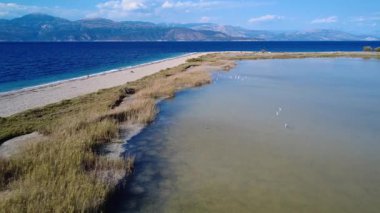 Yunanistan 'da bir sahil kenarındaki bir göl Akbalıkçıllar gibi nadir bulunan kuşları barındırır. Kuşlar çamurlu yüzeyde sakince dinlenirler. Bu da burayı hem kuş gözlemcileri hem de yüzücüler için bir yer yapar. Uçsuz bucaksız mavi deniz ve dağlar muhteşem bir Akdeniz zeminini oluşturur..