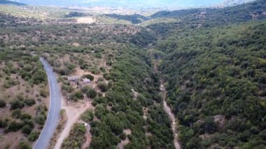 Yunanistan 'ın kırsal kesiminde, sıcak Akdeniz ışığının Avrupa' nın uzak nehrine ulaştığı kırsal bir bölgede terk edilmiş binaları bulunan eski bir otoyolun yanında çalılar, otlar ve küçük ağaçlarla dolu kayalık bir vadi bulunuyor..