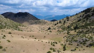 Dağların eteklerinde köknar ağaçları büyüdükçe dağlar arasında geniş bir ova uzanır. Yoğun bulutlar zirveyi gizliyor ve Yunanistan ve Avrupa 'nın sakin bölgelerine gölge düşürüyor.