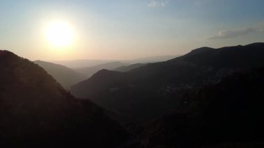 Güneş batarken ve ufuk bulanıklaşırken, sessiz bir vadideki engin uçurumlar arasında dev bir güneş alçalıyor. Son sıcak ışık Avrupa ve Yunanistan 'daki engebeli manzaraya temas ediyor.