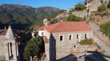 Demirden haçlı geleneksel Ortodoks çan kulesi sabah vakti bir Yunan dağ köyünde sergilenir. Yunanistan ve Avrupa genelinde yakın ev ve oteller görülüyor.