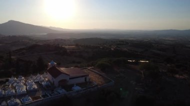 Batan güneş, bir tepedeki geleneksel bir mezarlıktan görünen açık ovanın üzerinde büyük görünür. Sessizlik ve yalnızlık, Yunanistan ve Avrupa 'daki kırsal manzarayı tanımlıyor.