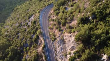 Yunanistan 'da köknar ormanı ve Akdeniz bitkisini geçen Avrupa dağlarının ulusal asfalt yolunun hava manzarası, dik kayalık yamaç gölgeleri, geçen bir araba dışında trafik hareketi yok. Görünür beyaz. Geçiş çizgileri ve uçuruma doğru güvenlik engelleri yok..