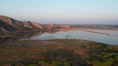 Durgun göl suları tepeleri, seyrek ağaçları ve yumuşak akşam ışığı altındaki bataklık bitkilerini yansıtır. Yunanistan ve Avrupa 'da sessiz doğal sulak arazi manzarası.