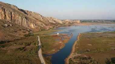 Küçük beyaz bir Ortodoks şapeli, kızıl bataklık bitki örtüsü ve kayalık kayalıklarla çevrili sakin göl sularına yansıyor. Yunanistan ve Avrupa 'da sakin doğal sulak arazi manzarası.