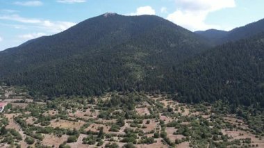 Köknar ormanlarıyla kaplı yüksek bir dağ geniş kuru tarlaların ve çalıların üzerinde yükselirken, Yunanistan ve Avrupa 'da bir otoyol ormanlık yamaçları geçiyor..