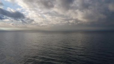 Sis uzak ufku yumuşatırken, bulutlu gri bir gökyüzü altında hafif dalgalarla sakin deniz tipik bir sonbahar ya da kış deniz manzarası yaratıyor..