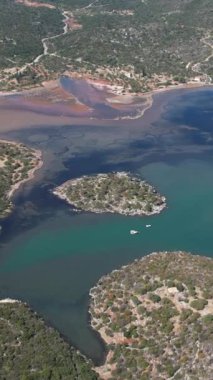 Panoramik hava görüntüsü, sığ kristal berrak su ve engebeli kıyı şeridi olan sessiz bir körfezde dinlenen küçük bir ada gösteriyor. Balıkçı tekneleri ve Akdeniz bitkileri Yunanistan ve Avrupa 'da sakin bir kıyı manzarasını ön plana çıkardılar.