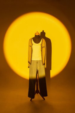 Büyük daireler çizen sarı ışıklı bir fotoğraf, gündelik kıyafetler giyen bir kadın mankeni gösteriyor.. 