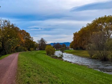 Günbatımından kısa bir süre önce geniş açılı sonbahar manzarası çekildi. Çalkantılı, dalgalı bir nehir çerçevenin sağ tarafını kaplar. Solda mükemmel manikürlü, parlak yeşil bir kıyı var. Gri-mavi gökyüzü ve bulut kümeleriyle çelişiyor.
