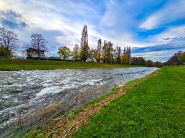 Günbatımından kısa bir süre önce geniş açılı sonbahar manzarası çekildi. Çalkantılı, dalgalı bir nehir çerçevenin sağ tarafını kaplar. Solda mükemmel manikürlü, parlak yeşil bir kıyı var. Gri-mavi gökyüzü ve bulut kümeleriyle çelişiyor.