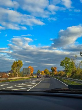 Olgun bir mısır tarlasını geçip kırsal bir asfalt yolda giden bir arabadan bakış açısı. Siyah bir araba bulutlu güzel bir gökyüzünün altında uzak dağlara doğru yol alıyor..