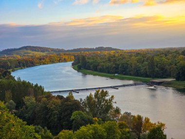 Ren Nehri 'nin sonbahar ormanları ve tepeler boyunca akan manzarası. Görüntü, altın bir günbatımı gökyüzünü yansıtan bir nehir ve sakin bir suyu yansıtır. Avrupa 'da sonbahar sezonunda yüksek bir bakış açısıyla ele geçirildi.