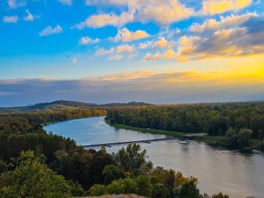 Ren Nehri 'nin sonbahar ormanları ve tepeler boyunca akan manzarası. Görüntü, altın bir günbatımı gökyüzünü yansıtan bir nehir ve sakin bir suyu yansıtır. Avrupa 'da sonbahar sezonunda yüksek bir bakış açısıyla ele geçirildi.
