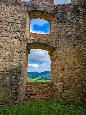 Hochburg Kalesi 'nin (Emmendingen, Almanya) korunmuş Gotik pencere açıklarından geçen Kara Orman manzarasının pitoresk bir görüntüsü. Güneş ışığı, yemyeşil bir vadinin arka planına karşı kırmızı kumtaşı dokusunu vurgular.