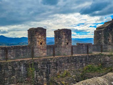 Hochburg Kalesi 'nin tarihi taş duvarlarının ve kulelerinin dramatik bulutlu gökyüzünün altında panoramik bir görüntüsü. Harabeler, Almanya 'daki Kara Orman' ın uzak mavi dağlarına bakıyor..