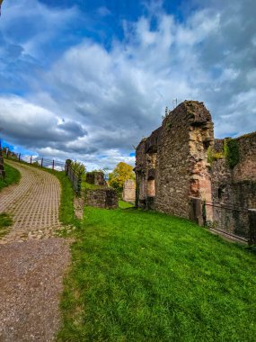 Hochburg Kalesi 'nin yüksek ortaçağ duvarlarının geniş açılı görüntüsü. Geleneksel bir kaldırım taşı yolu, Kara Orman bölgesinde dramatik bir gökyüzüne karşı inşa edilen muazzam tahkimatların yanında yer alıyor..