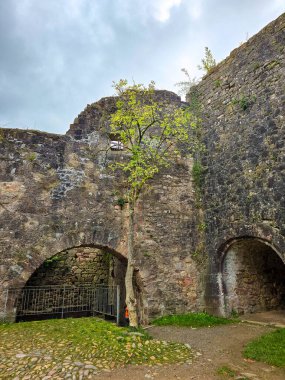 Hochburg Kalesi 'nin yüksek ortaçağ duvarlarının geniş açılı görüntüsü. Geleneksel bir kaldırım taşı yolu, Kara Orman bölgesinde dramatik bir gökyüzüne karşı inşa edilen muazzam tahkimatların yanında yer alıyor..