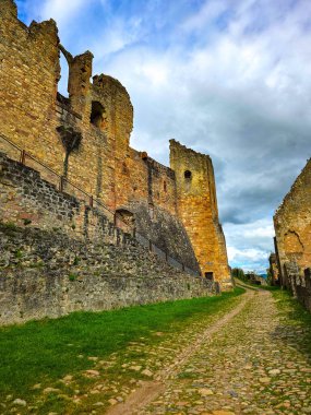 Hochburg Kalesi 'nin yüksek ortaçağ duvarlarının geniş açılı görüntüsü. Geleneksel bir kaldırım taşı yolu, Kara Orman bölgesinde dramatik bir gökyüzüne karşı inşa edilen muazzam tahkimatların yanında yer alıyor..