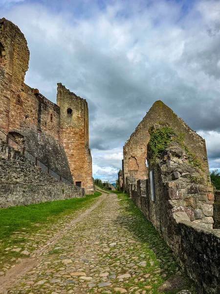 Hochburg Kalesi 'nin yüksek ortaçağ duvarlarının geniş açılı görüntüsü. Geleneksel bir kaldırım taşı yolu, Kara Orman bölgesinde dramatik bir gökyüzüne karşı inşa edilen muazzam tahkimatların yanında yer alıyor..