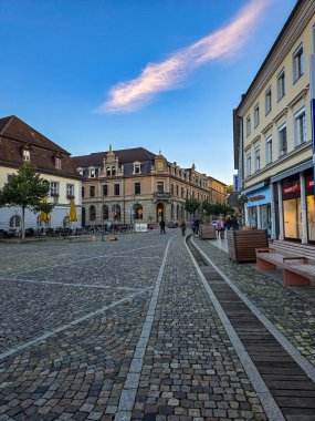 Weiden, der Oberpfalz, Bavyera 'daki Yukarı Pazar Meydanı' nın pitoresk bir akşam manzarası. Tarihi Hotel Post binası, yerel dükkanlar ve açık mavi gökyüzünde çarpıcı bir pembe gün batımı bulutu. Geleneksel Alman kasaba mimarisi