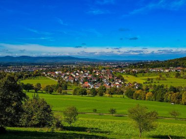 Kara Orman Almanya 'sında kayan tepeleri ve mavi dağları olan pitoresk yeşil çayırlar ön planda yemyeşil eğimli çayırlar ve arka planda bulutlu bir gökyüzünün altında görkemli mavi dağ sıraları vardır.
