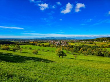 Kara Orman Almanya 'sında kayan tepeleri ve mavi dağları olan pitoresk yeşil çayırlar ön planda yemyeşil eğimli çayırlar ve arka planda bulutlu bir gökyüzünün altında görkemli mavi dağ sıraları vardır.