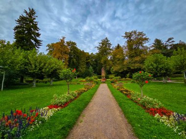 Yeşil ağaçların arasına yerleşmiş geleneksel ahşap bir çardağın yer aldığı Avrupa parkının güzel bir manzarası. Ön planda düzgün budanmış çalılar, küresel çalılar ve bahçe yolları bulutlu bir günde huzurlu ve sakin bir atmosfer yaratıyor..