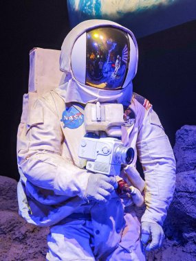 NASA uzay giysisi giymiş bir astronot elinde eski model bir kamera, arkasında da Dünya var. Görüntü uzay giysisinin detaylarını vurgular, uzayda bir keşif ve macera ruhunu yansıtır.