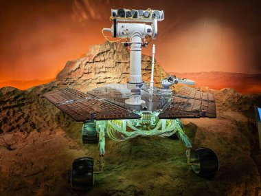 Mars 'ın engebeli tekerleklerini, güneş panellerini, sensörlerini ve arka plandaki kırmızı çölü vurgulayan, uzay keşiflerini ve gelişmiş teknolojiyi anımsatan bir NASA aracının ayrıntılı görüntüsü..