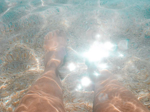 Vacation at sea. Turquoise clear water, sand, reflection of the sun\'s rays. Female feet close up in clear water