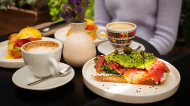 Somon ve avokado ile güzel dekore edilmiş tost, yumurtalı benedict ve cappuccino Kahvaltı toplantılar için gidiş zamanıdır. 