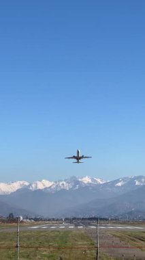 Açık mavi gökyüzünün altında, karlı dağ sırasına doğru uçan uçak.