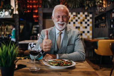 Restoranda oturup yemek yiyen mutlu bir iş adamı. Lezzetli yemek ve şarabın tadını çıkarıyor..