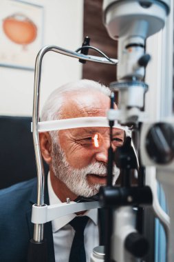 Optalmoloji tedavisi gören zarif yaşlı sakallı adam. Doktor göz doktoru gözlerini modern ekipmanlarla kontrol ediyor..