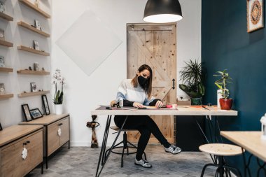 Stüdyosunda ya da atölyesinde çalışan kağıt tasarımcısı ve sanatçı. Virüs salgınına karşı koruyucu yüz maskesi takıyor..