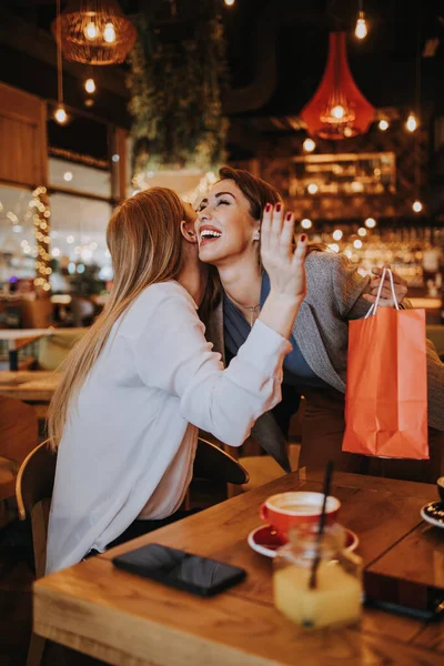 Two best friends meet in a nice restaurant or coffee bar. One prepares a surprise for the other and gives her a birthday present. Happy young people.