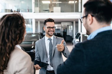 Araba galerisinden araba alan orta yaşlı bir çift. Araba satıcısı doğru karar vermelerine yardımcı oluyor..