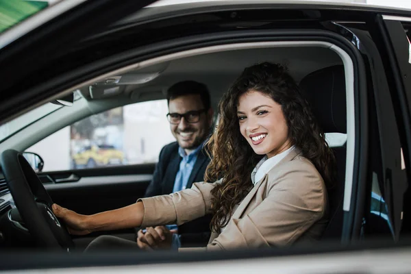 Happy middle age couple enjoying while choosing and buying new car at showroom.