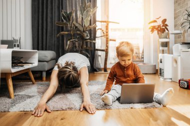 Güzel, genç bir anne, sevimli oğluyla egzersiz yapıyor ve yoga yapıyor. Eğleniyorlar, oynuyorlar ve gülümsüyorlar..