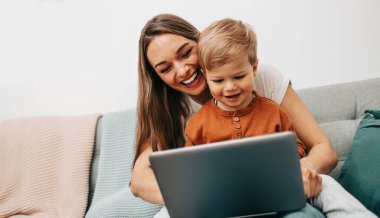 Küçük oğluyla mutlu bir anne online alışveriş yapıyor ya da evden çalışıyor. Mesafeden iş ve sanal iletişim.