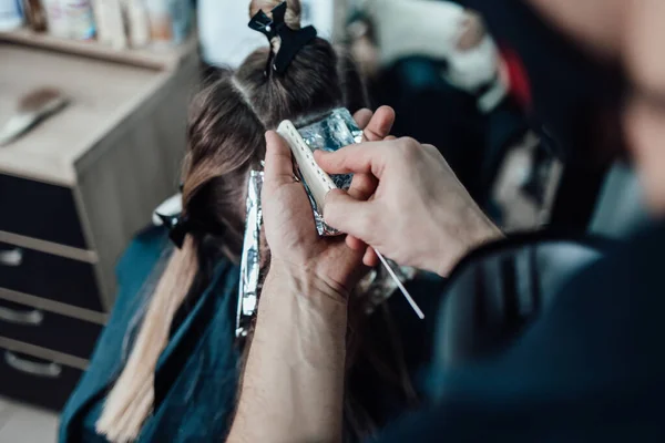 Hairdresser is dyeing female hair, making hair highlights to his client with a foil.