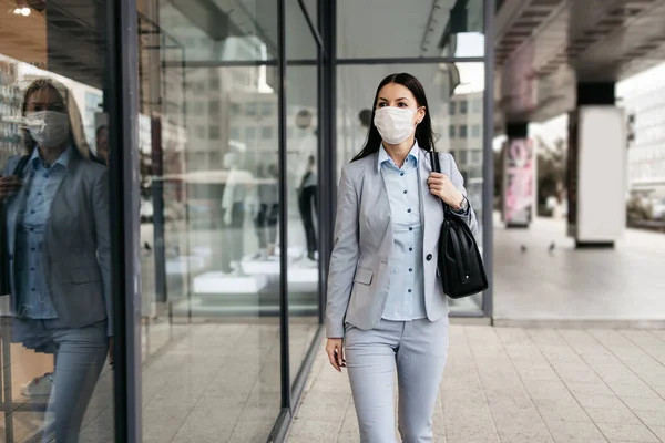 Young and elegant business woman standing on empty city street and wearing protective mask to protect herself from dangerous flu or virus. Corona virus or Covid-19 concept.