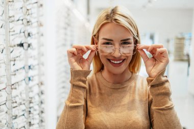 Modern optik mağazada gözlük çerçevesi seçen güzel ve şık bir kadın..