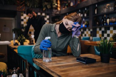 Genç restoran çalışanları Coronavirus salgınına karşı masaları temizleyip dezenfekte ediyorlar. Koruyucu maske ve eldiven takıyorlar..