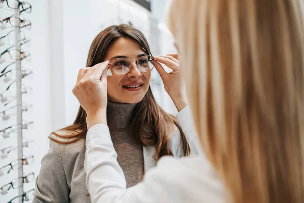 現代の光店で眼鏡フレームを選択する美しくファッショナブルな女性 女性の売り手の専門家は彼女が正しい決定を下すのを助ける — ストック写真