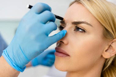 Muayene odasında yüz hatları ve noktalarında düzeltme çizgileri olan güzel bir bayan hasta..