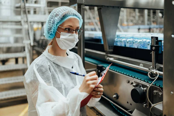 在医疗用品研究和生产工厂工作的带防护面罩的女工 在装运前检查蒸馏水罐 检查质量控制 — 图库照片