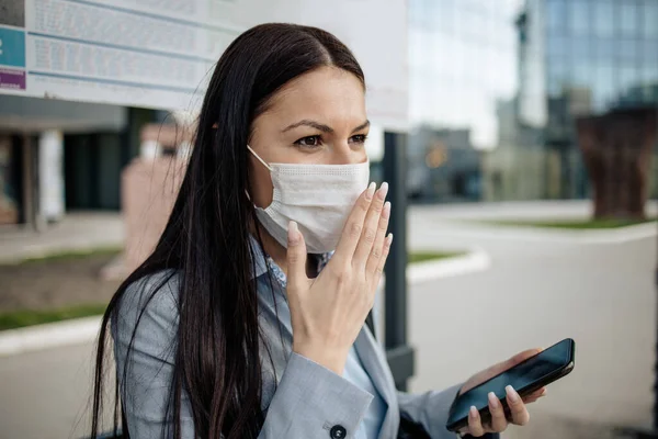 Elegant business woman infected and sick by virus standing on city street with protective mask, coughing and sneezing. Corona virus or Covid-19 lifestyle concept.