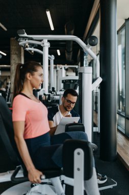 Modern spor salonunda spor yapan genç ve çekici bir kadın. Kişisel fitness hocası veya koçuyla birlikte..